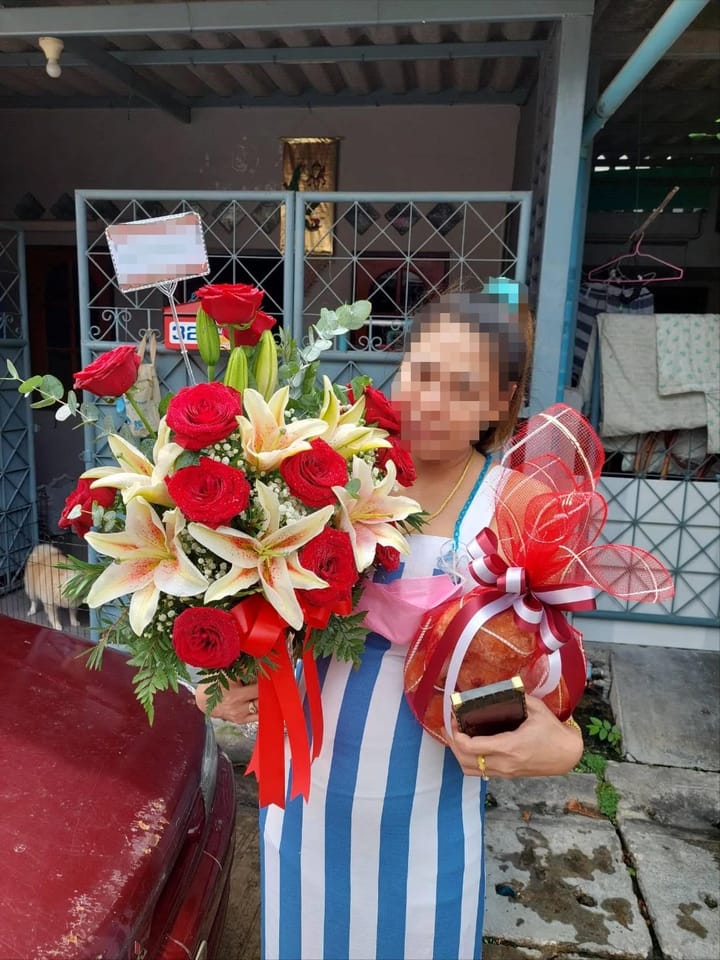 ลูกค้ากำลังรับแจกันดอกไม้ที่คล้ายกัน มีกุหลาบแดง ลิลลี่ครีมและชมพู ยิปโซขาว ใบยูคาลิปตัส พร้อมผลไม้ (สินค้าอื่น)
