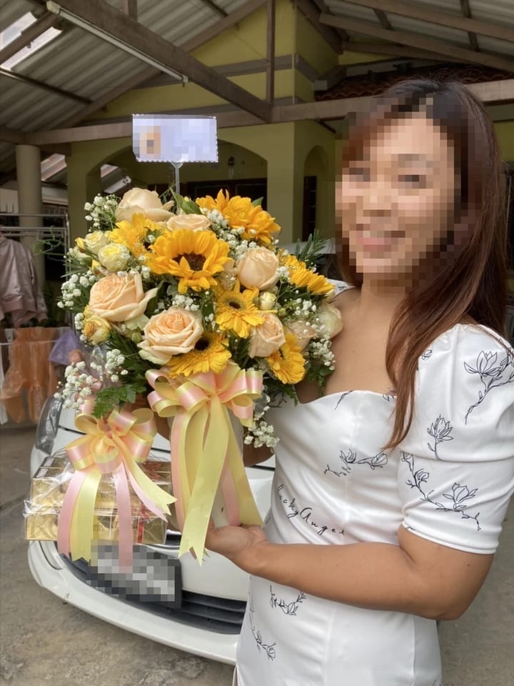 ลูกค้ากำลังรับแจกันดอกไม้ที่คล้ายกัน มีทานตะวันเหลือง กุหลาบพีชและครีม เยอบีร่าเหลือง ยิปโซขาว พร้อมช็อกโกแลต (สินค้าอื่น)